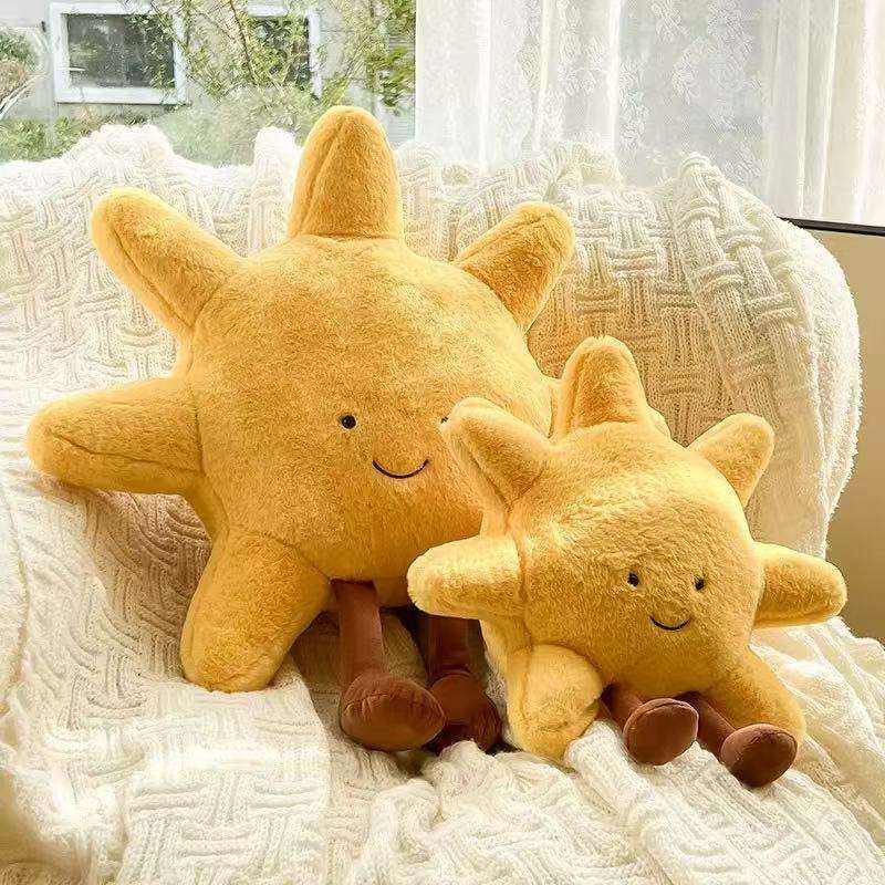 Two yellow smiling sun plush pillows in large and small sizes on a white blanket.