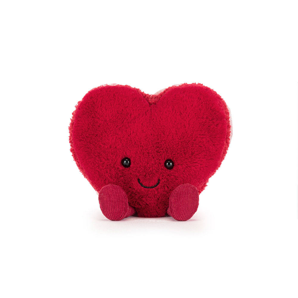 A fluffy red heart-shaped macaron plush toy with a cute smiling face and tiny legs sitting on a white background.